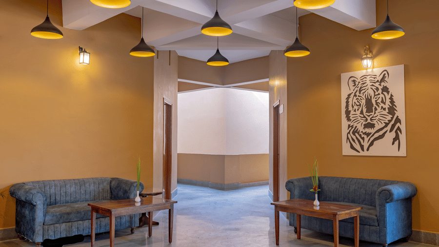 A lobby area at Estherea Bagh, Ranthambore, with tan walls, 2 upholstered sofas, pendant lights, and a large tiger art print.