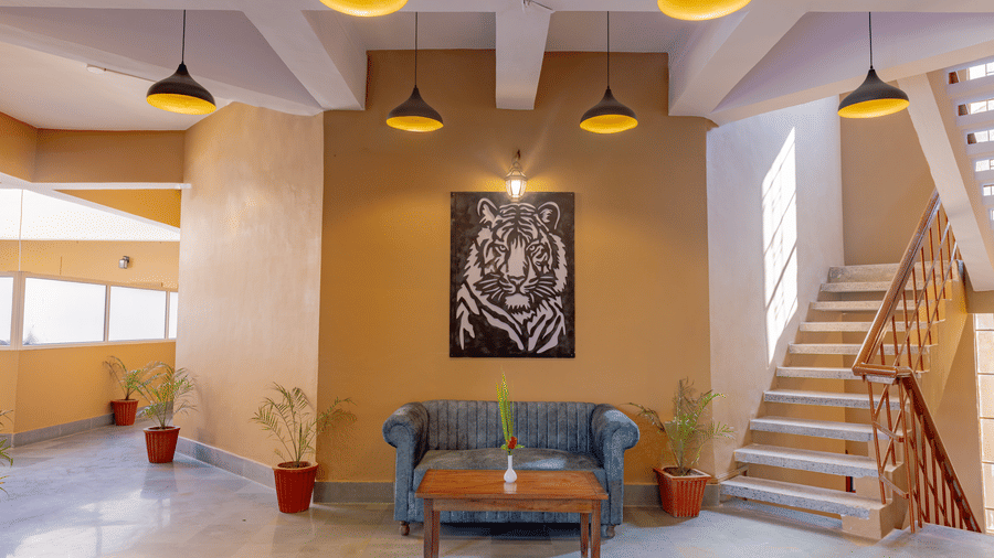 A lounge space at Estherea Bagh, Ranthambore, with a sofa, a tiger print, and a staircase under warm pendant lights.