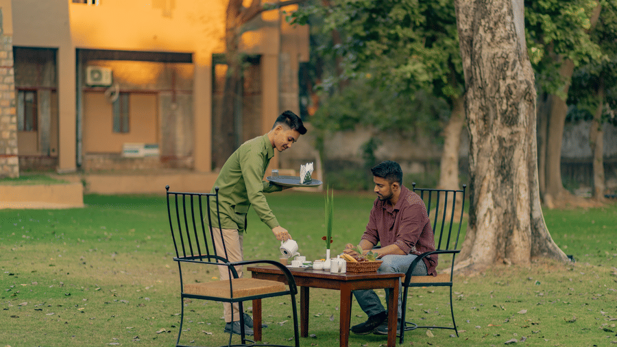 A staff member serving 2 people at a small table on the grassy lawn at Estherea Bagh, Ranthambore.