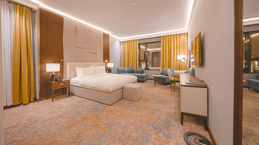 Junior Suite bedroom at Grand Iva Hotel, Abha, showcasing the spacious layout furnished with a plush double bed facing a wall-mounted TV placed beside a seating area.