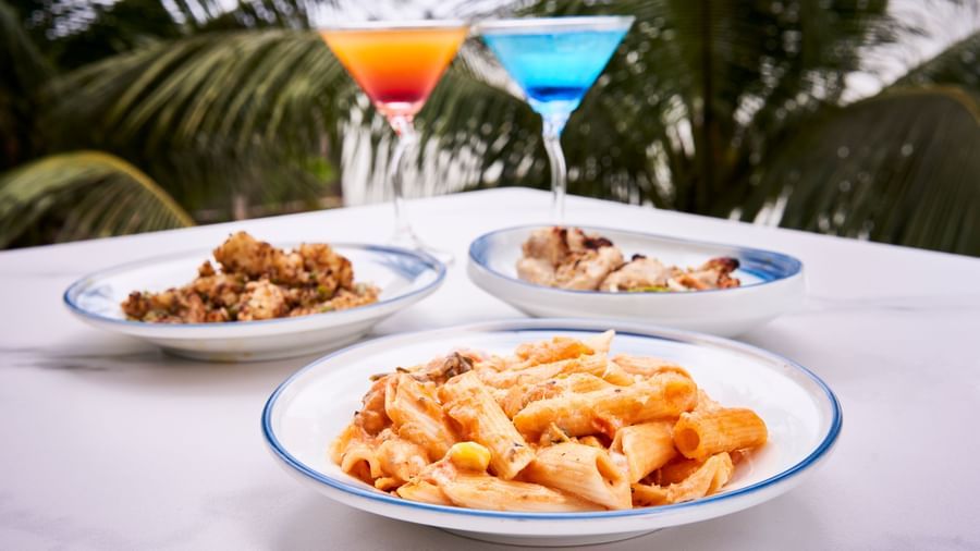 Plates of pasta, curry, and roasted chicken with cocktails in the background.