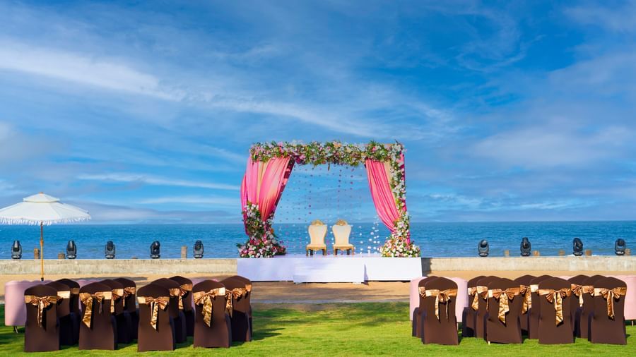 Outdoor lawn with decorated chairs, platform stage decorated with flowers & the view of the blue sky & sea at Grande Bay Resort & Spa.