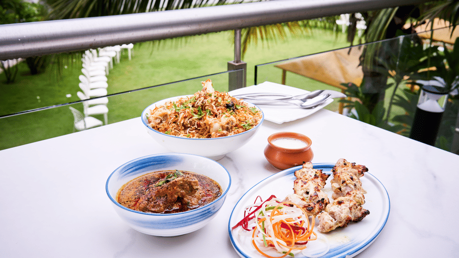 Outdoor dining setup featuring biryani, curry bowl, and grilled kebabs served on a white table - Grande Bay Resort & Spa, Mamallapuram