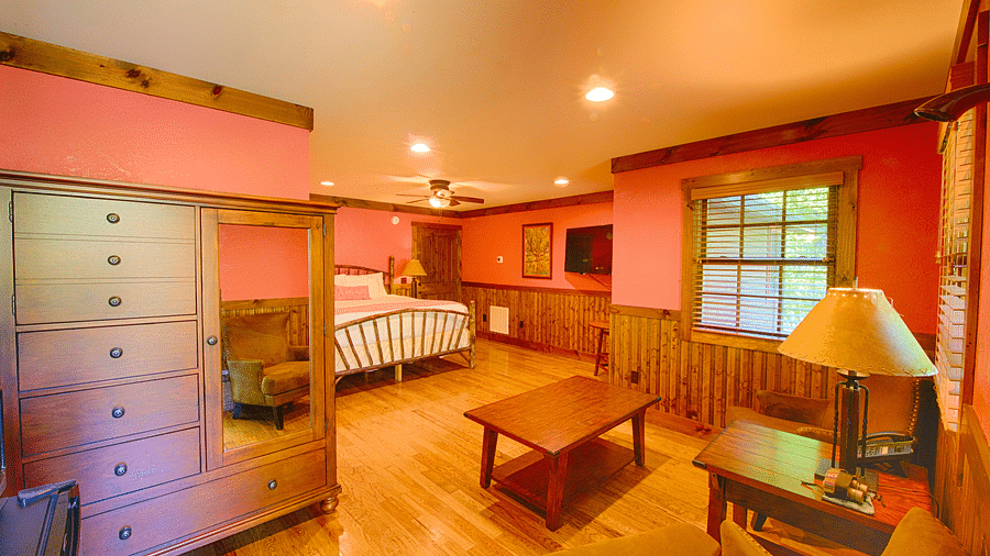 corner view image of a bedroom with a wardrobe and common seating area and a double bed at the far end - Historic Tapoco Lodge
