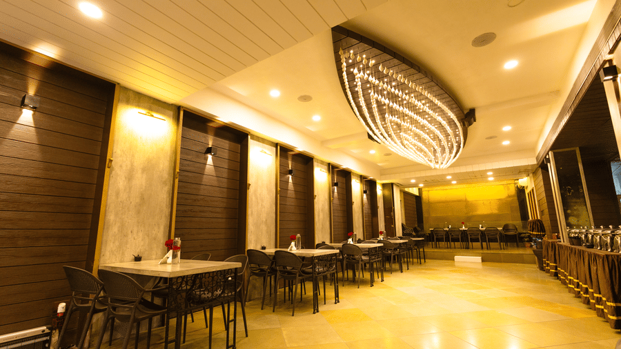 An indoor dining area with dining tables, chairs, and ceiling lights at Hotel Seagull Digha.
