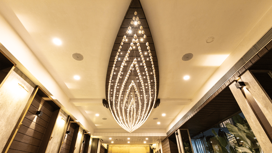 The ceiling view of the dining area at Hotel Seagull Digha showing a long decorative chandelier, lighting, and corridor walls on both sides.