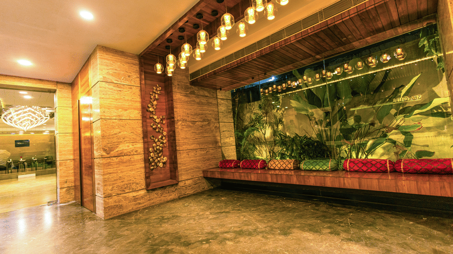 A seating area with a bench, cushions, plants, and overhead lights at Hotel Seagull Digha.