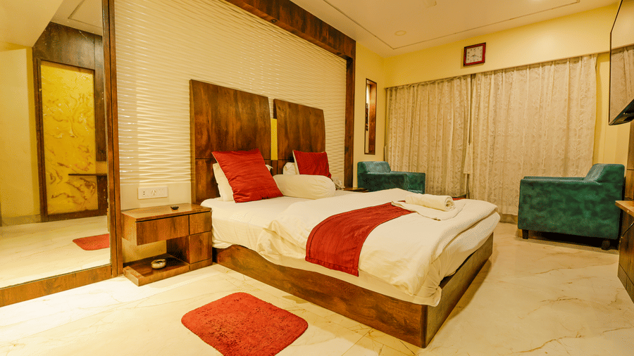 A bedroom with a king size bed, red cushions, a mirror, a bedside table and 2 armchairs at Hotel Seagull Digha.