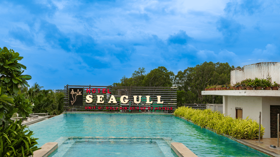 A swimming pool in front of the building with the ‘Seagull’ signage and trees in the background at Hotel Seagull, Digha.