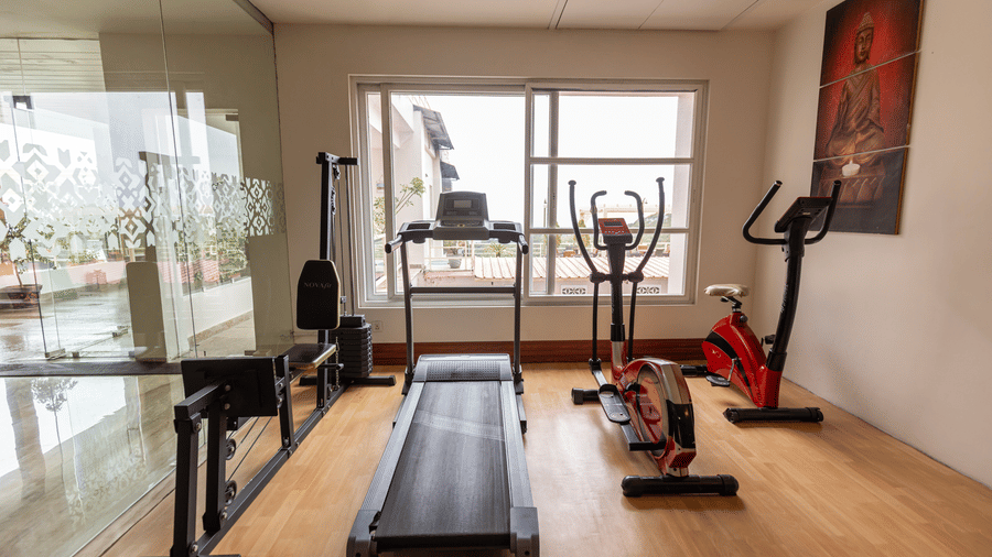 A gym with treadmills, exercise bikes, and glass windows allowing light inside at Indraprastha Resort & Spa, McLeod Ganj.