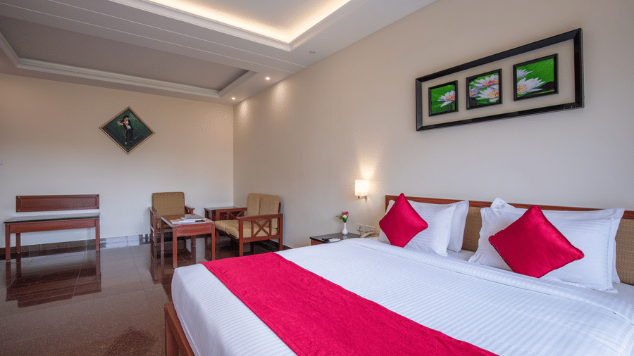 A comfortable hotel room with a large double bed, recessed ceiling lighting, and red accent pillows - Jenneys Residency, Coimbatore