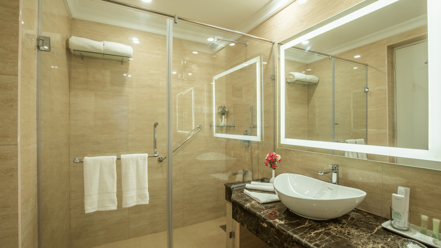 A clean modern bathroom featuring a glass-enclosed shower and a vanity with a large LED mirror - Jenneys Residency, Coimbatore