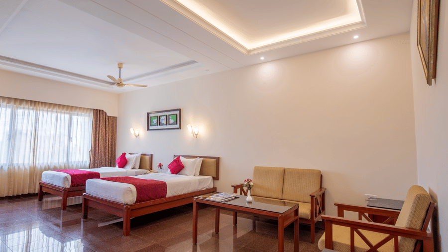 A large room featuring twin beds and a wooden sofa seating area for guests - Jenneys Residency, Coimbatore