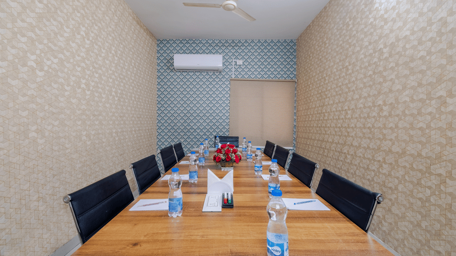 : A symmetric boardroom view at Lemonridge by Monday Hotels - Kukatpally showcases clear water bottles, paper pads, and black office chairs lining a long table.