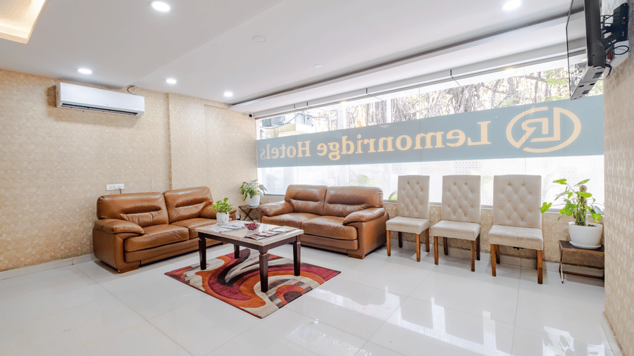 The indoor seating lounge at Lemonridge by Monday Hotels - Kukatpally features leather couches, individual chairs, tables, A/C, and window text.