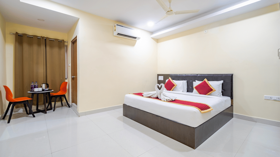 A room featuring a large bed, A/C, ceiling fan, 2 chairs, and a table in the corner at Lemonridge by Monday Hotels - Kukatpally.