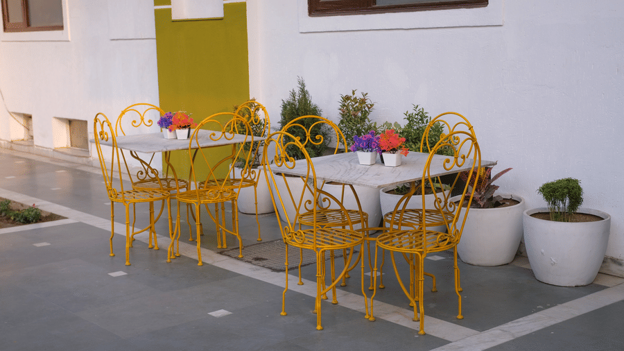 Outdoor seating area of Lime Tree Hotels & Service Apartment Private Limited featuring yellow chairs and round tables.