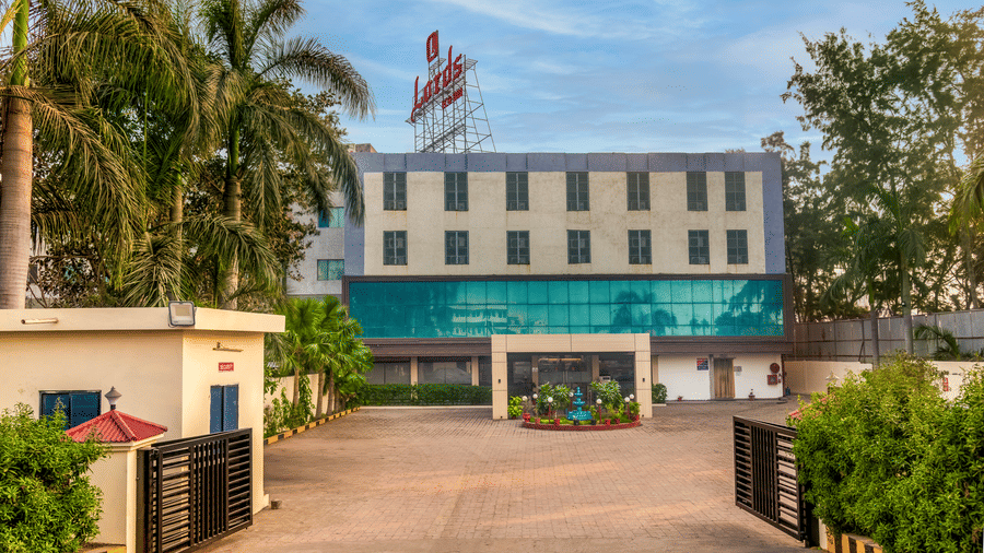  The exterior of a Lords Eco Inn hotel building with a green facade, an outdoor area, and flags on the roof.