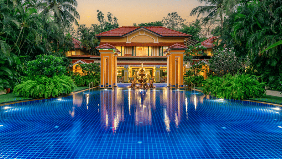 Stunning infinity pool at Mayfair Lagoon, Bhubaneswar, reflecting the illuminated hotel façade surrounded by lush tropical greenery at dusk