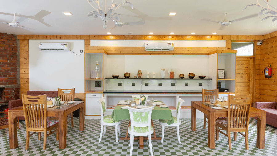An indoor dining space with wooden tables, green chairs, and a counter at the back - Megha Resort & Villas, Dehradun