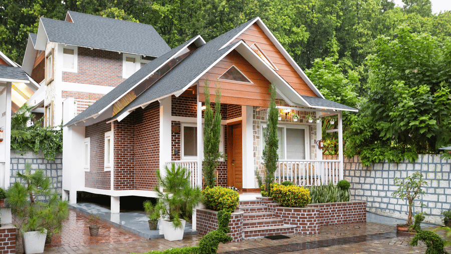A small house with a porch, green lawn, and surrounding trees on a cloudy day - Megha Resort & Villas, Dehradun