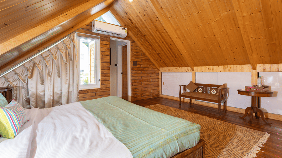 A unique attic bedroom with a bed, sloping wooden ceiling, and a textured stone feature wall at Megha Resort & Villas, Dehradun.