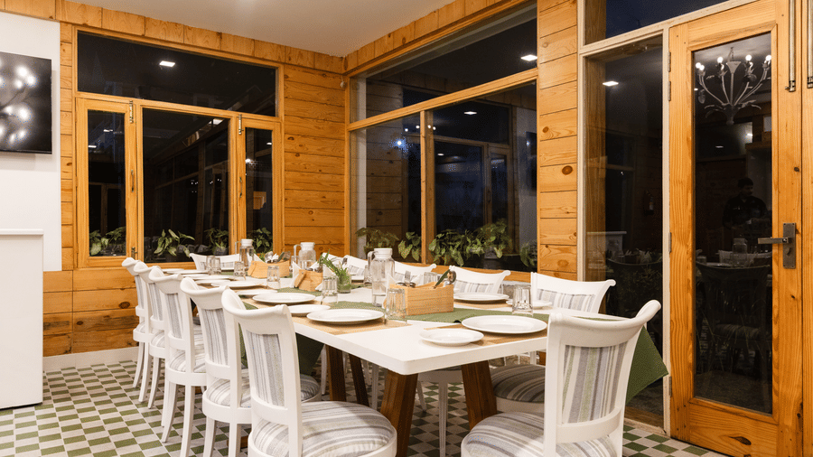 A brightly lit dining room with wooden panelling, doors, and a long table set with white chairs - Megha Resort & Villas, Dehradun