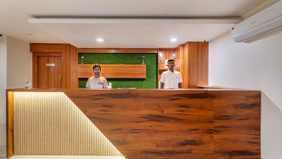 A hotel reception area with 2 people standing infront of the wooden desk under warm lighting - Monday Hotels HITEC City, Hyderabad