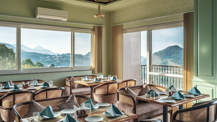 A dining space filled with natural light, chairs and tables are placed with cutlery and hand towels at Mountoria Retreat, Naukuchiatal