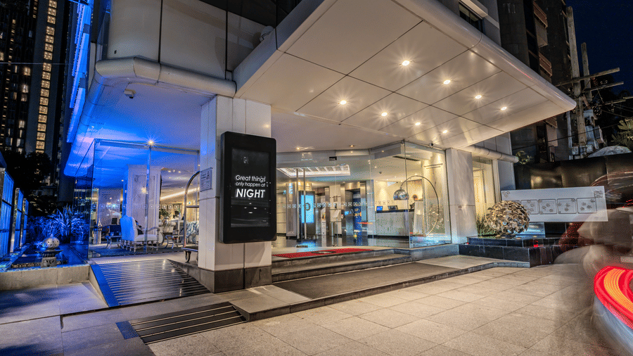 The entrance of one of the best hotels in Bangkok center, featuring bright exterior lighting, sleek modern architecture, glass lobby doors, and elegant nighttime ambiance | Night Hotel