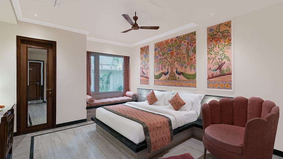 A spacious bedroom at Panna Vilas Palace, featuring a wooden table, cushioned furniture, warm lighting, and a large window