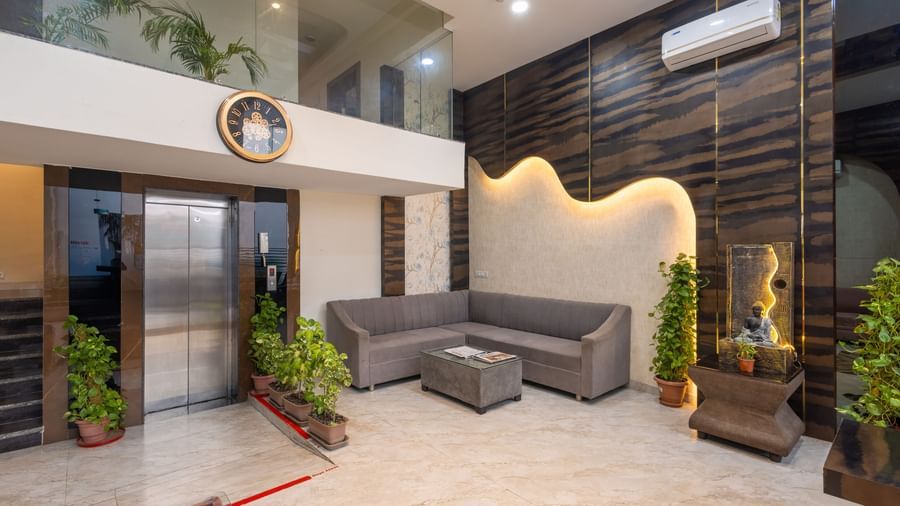 Seating area in a lobby with grey sofas, plants and stylish carved wall at Pravasa Stay Dewas Naka, Indore.