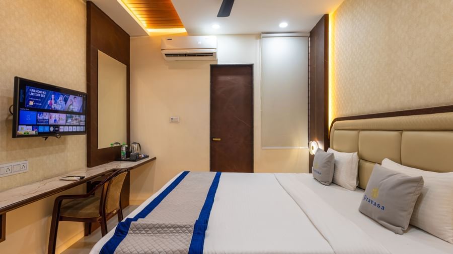 Room with a double bed, wall-mounted TV & a chair, and ceiling fan at Pravasa Stay Dewas Naka, Indore.