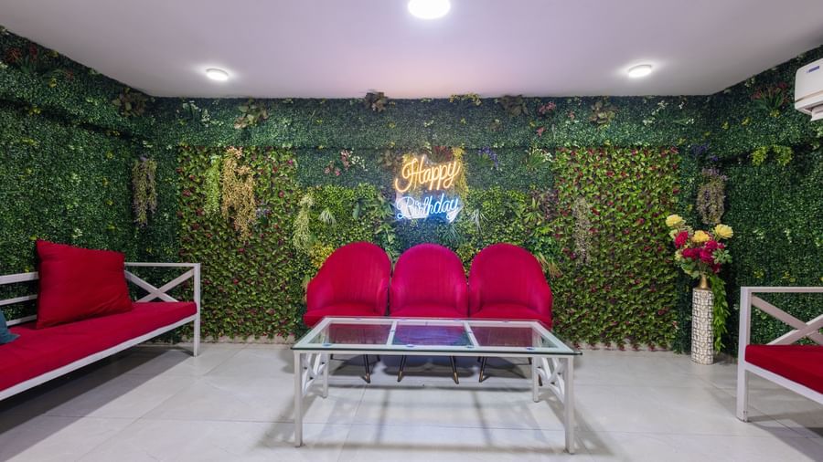 Seating lounge with red sofas, glass table, and green vertical garden wall at Pravasa Stay Dewas Naka, Indore.