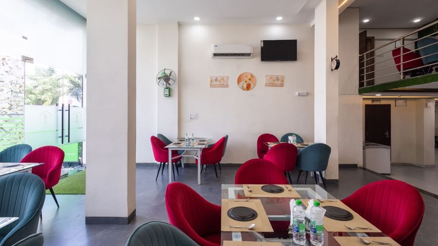 Indoor dining space with red and blue chairs around tables near glass doors at Pravasa Stay Dewas Naka, Indore.