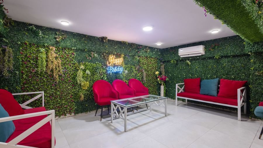 Lounge with red sofas, a glass table, and greenery-covered wall at Pravasa Stay Dewas Naka, Indore.