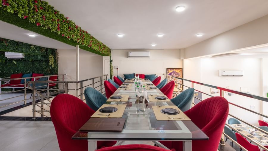 Long dining table setup with red & blue chairs and green decor on the wall at Pravasa Stay Dewas Naka, Indore.