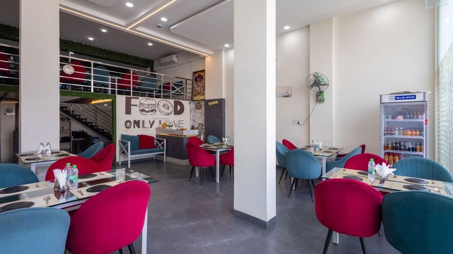 Indoor dining area with tables, red and blue chairs, and wall decor at Pravasa Stay Dewas Naka, Indore.