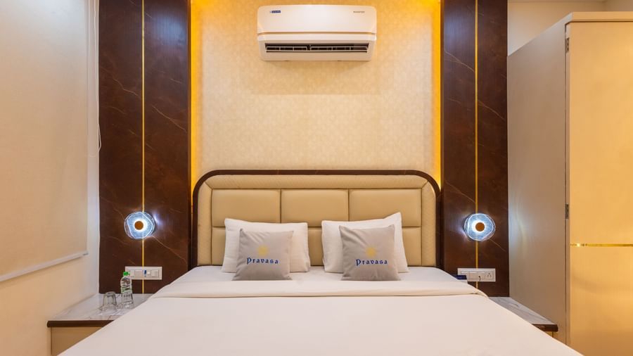 A double bed with a brown headboard, bedside lamps, and an air-conditioning  featuring warm lighting at Pravasa Stay Dewas Naka, Indore.