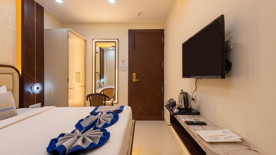 Room featuring a double bed, wall-mounted TV, a mirror with a chair, and wardrobe at Pravasa Stay Dewas Naka, Indore.