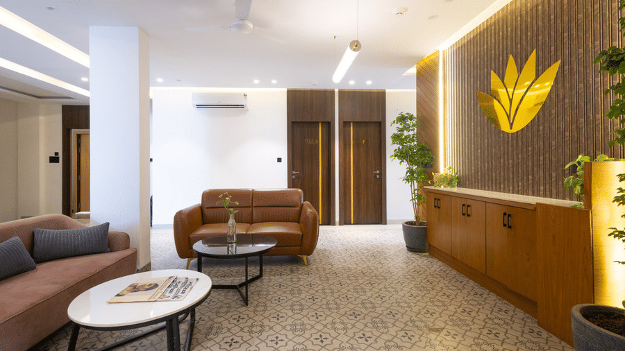 Interior view of the lobby area with seating around a coffee table and a decorative wall logo at Pravasa Stay Luv Kush, Indore.