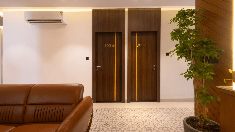 Interior view of the lobby area showing a brown sofa and a plant next to a wooden door at Pravasa Stay Luv Kush, Indore.