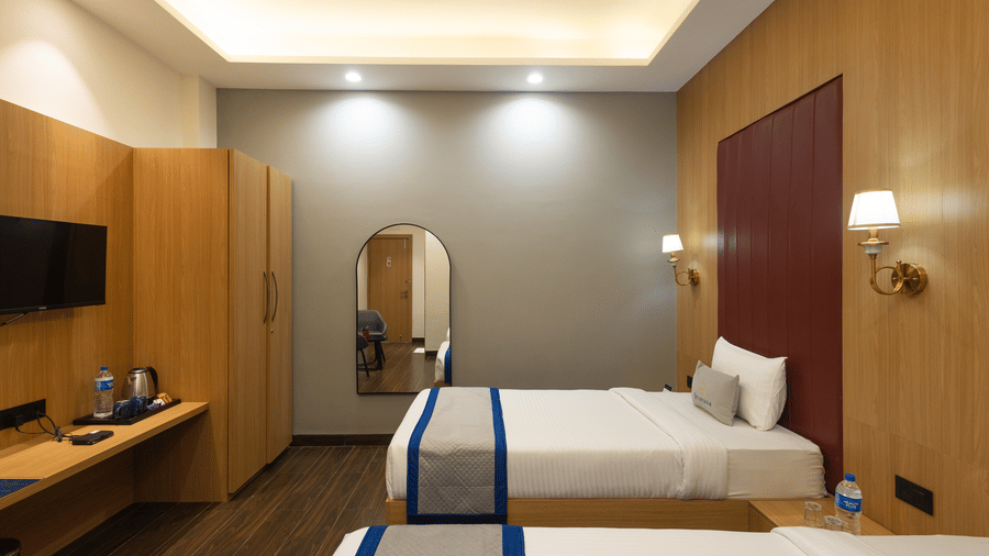 Interior of a guest room showing a twin beds, television, and desk at Pravasa Stay Luv Kush, Indore.