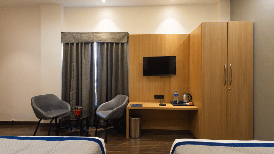Interior view of a guest room showing 2 single beds, chairs, and a desk area at Pravasa Stay Luv Kush, Indore.