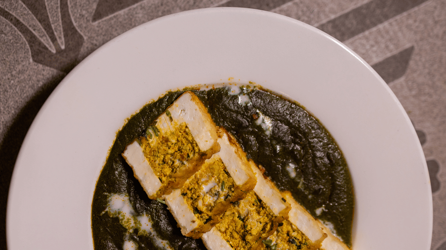 Close-up view of a plate of paneer or cheese in a green curry sauce at Pravasa Stay Luv Kush, Indore.