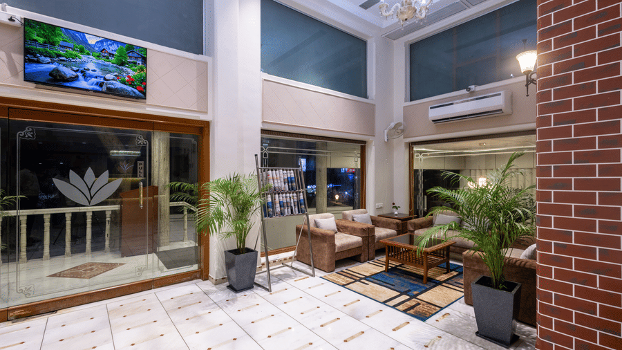View of a patio/courtyard area with seating and plants, looking towards the hotel interior through glass doors at Pravasa Stay, Vadodara.