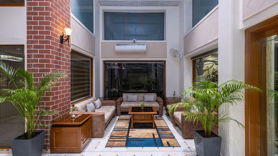Outdoor courtyard seating with modern furniture, a water feature, and a view of the hotel's brick walls and interior at Pravasa Stay, Vadodara.