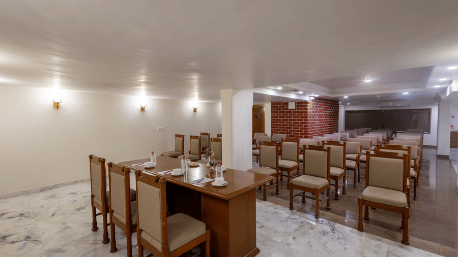 Dining room with wooden tables, chairs, and neutral walls, set for a meal in a simple, well-lit setting at Pravasa Stay, Vadodara.