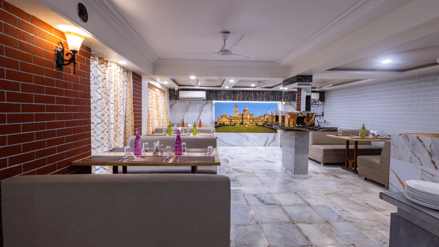 Spacious, brightly lit restaurant interior with neutral-toned seating, exposed brick wall accents, and marble flooring at Pravasa Stay, Vadodara.