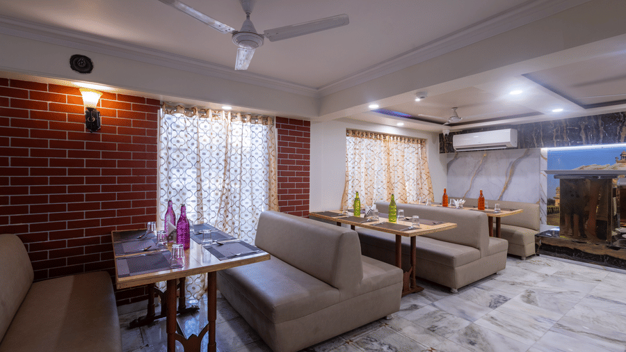Corner of a restaurant with soft sofa seating, a coffee table, a ceiling fan, and red brick wall detailing at Pravasa Stay, Vadodara.